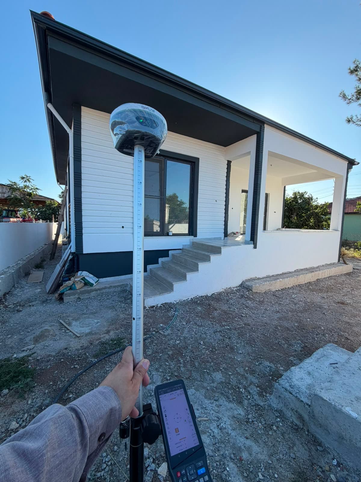 Yeni yapılmış bir evin önünde GNSS anteni ve el terminaliyle yapılan aplikasyon ölçümü